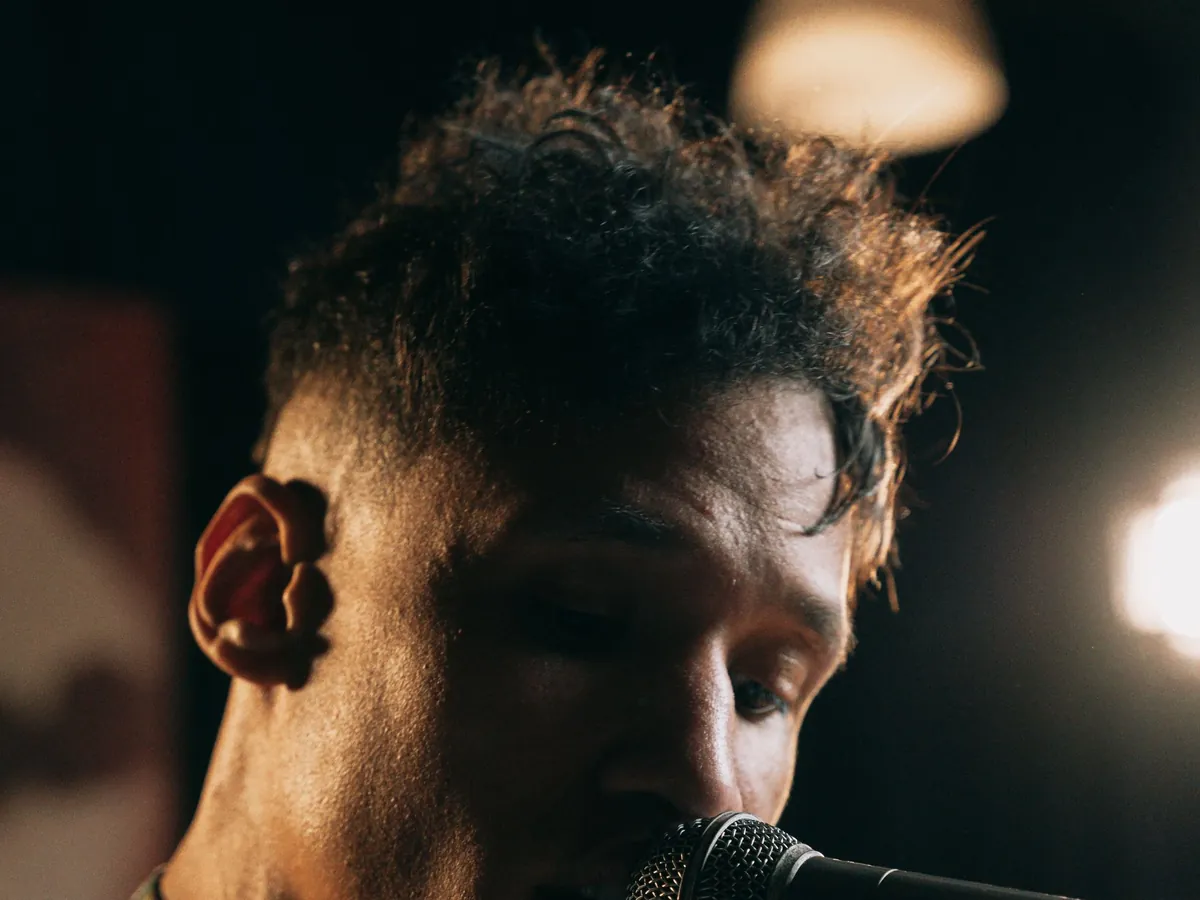 Curly-haired young man singing with his head bowed in a dim club