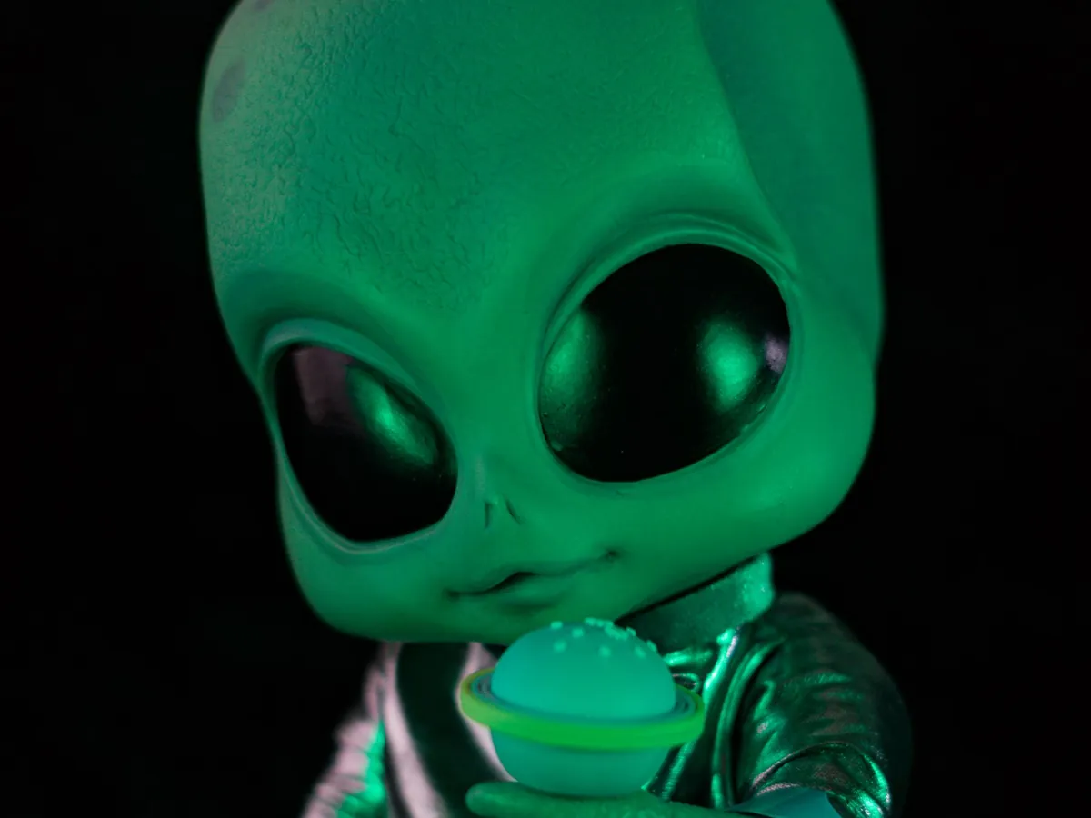 Green toy alien with big black eyes glowing in the dark