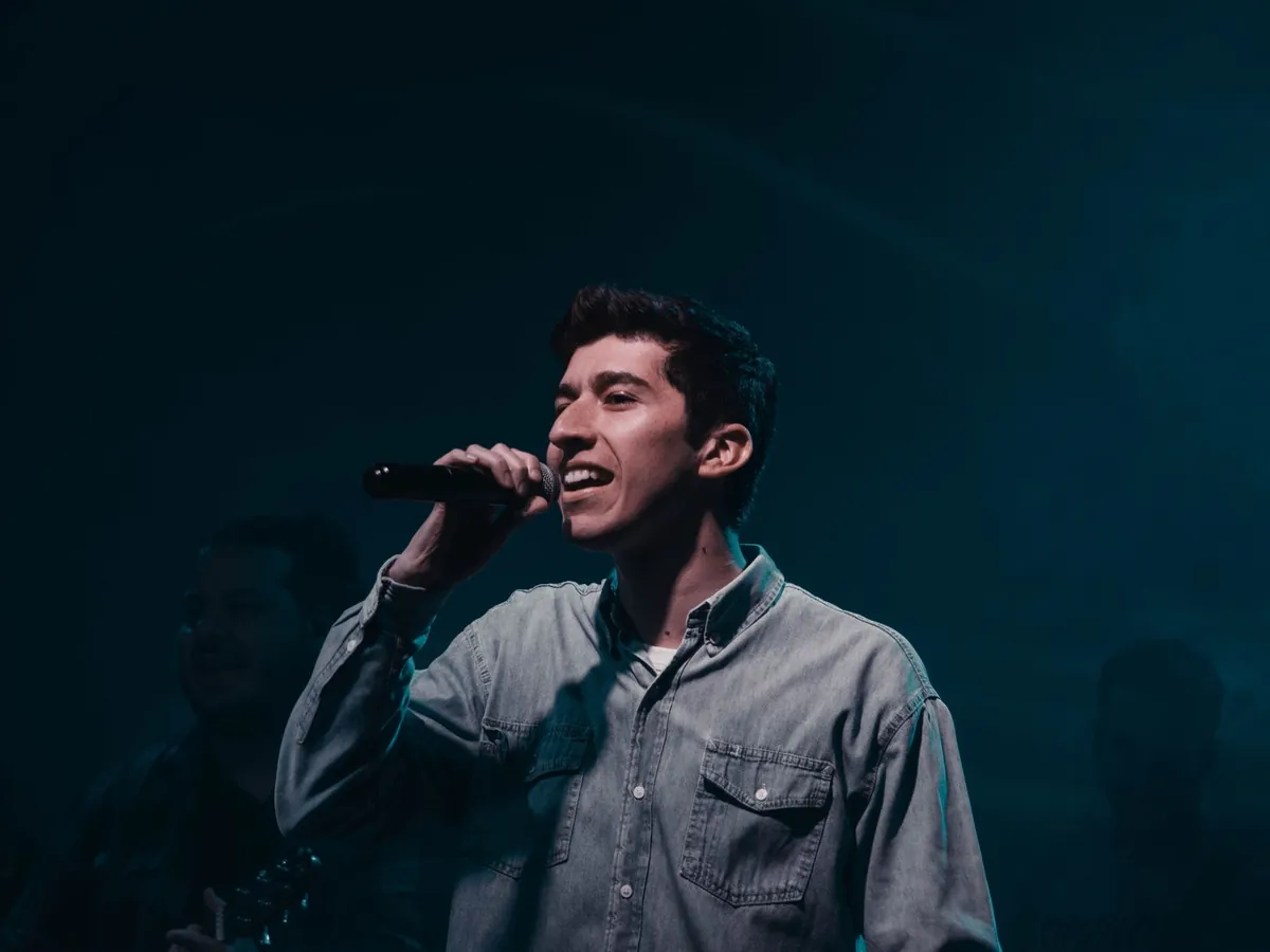 Man singing into a microphone on a dark stage lit in blue