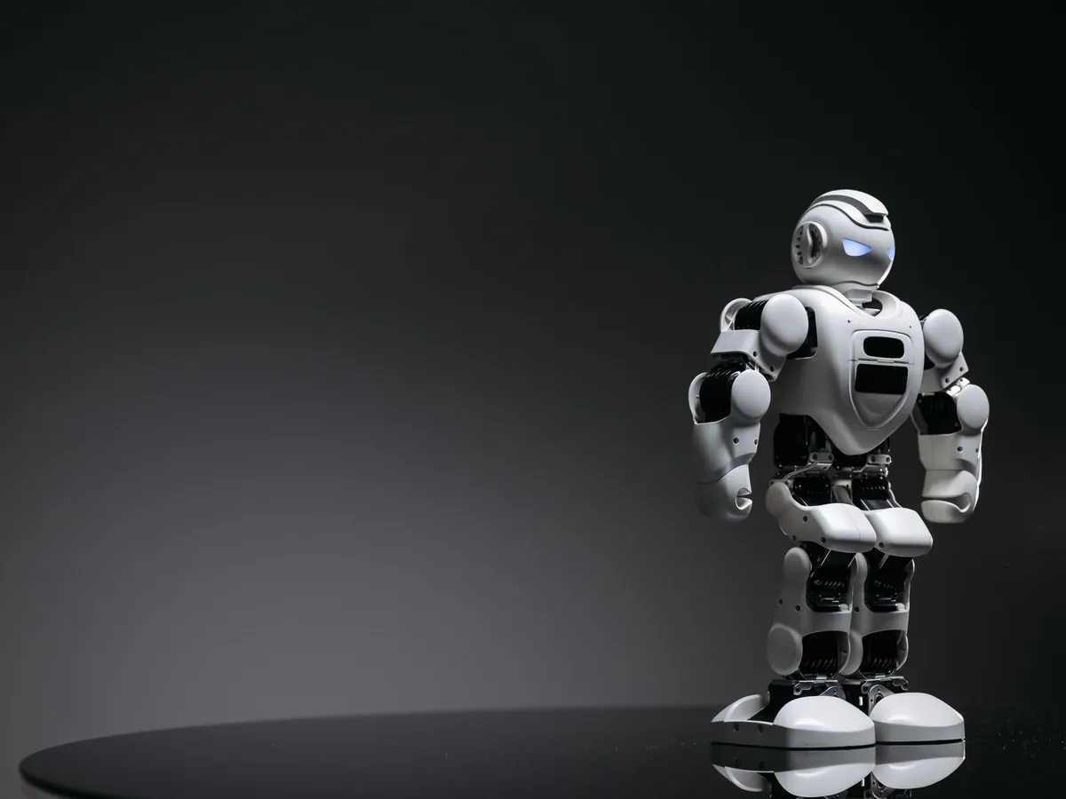 Small white robot standing alone on a dark stage