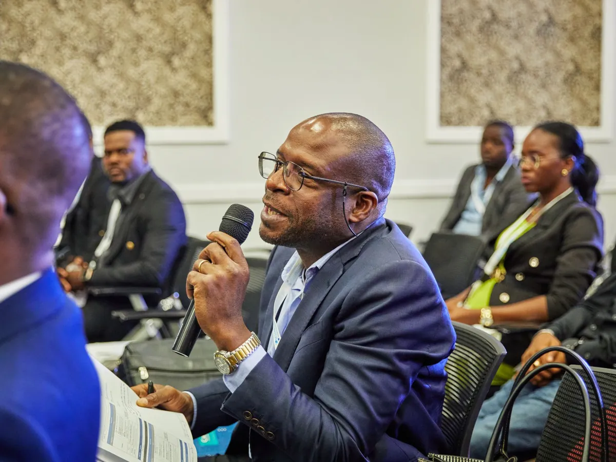 Man speaking into a microphone from his seat at a packed conference