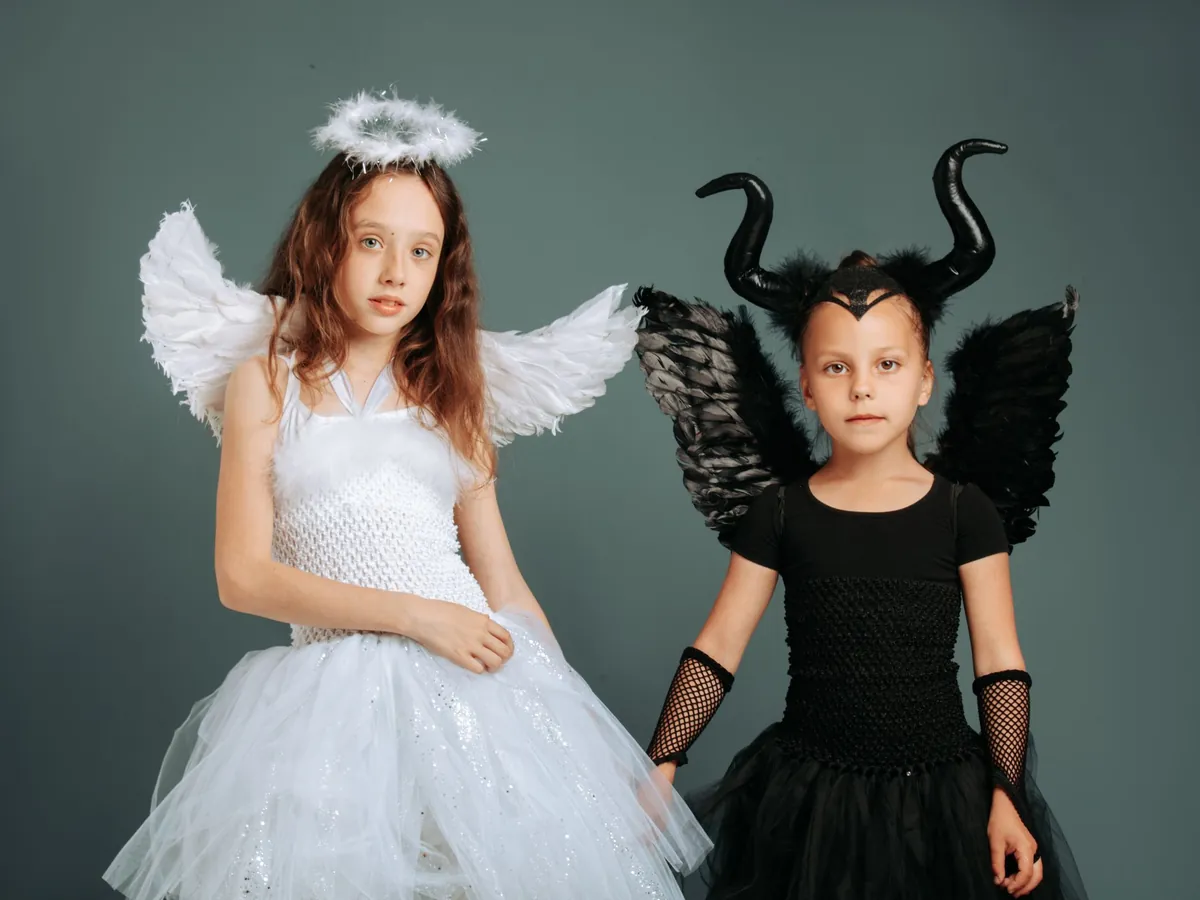 Two kids dressed as an angel and a horned dark fairy, ready to play their characters