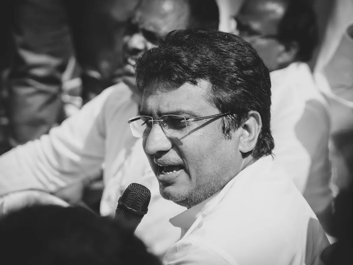 Man in glasses speaking into a microphone, in a black-and-white photo
