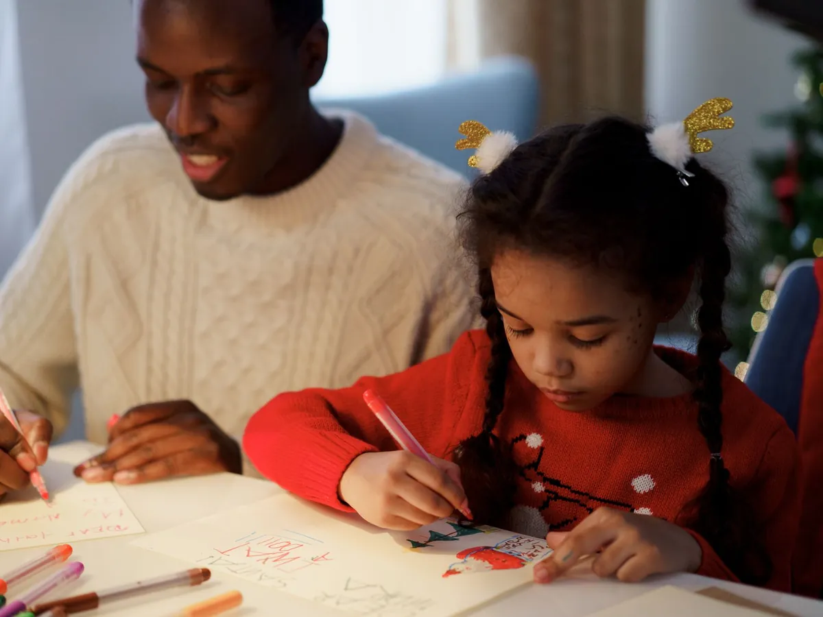 Dad helping his daughter write a letter to Santa at the table