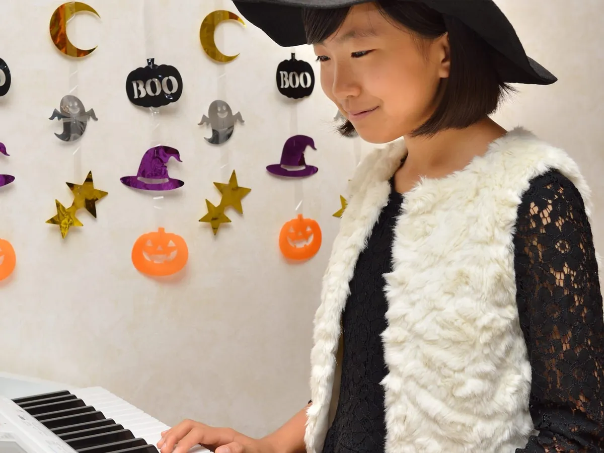 Girl in a witch hat playing a keyboard in front of Halloween decorations