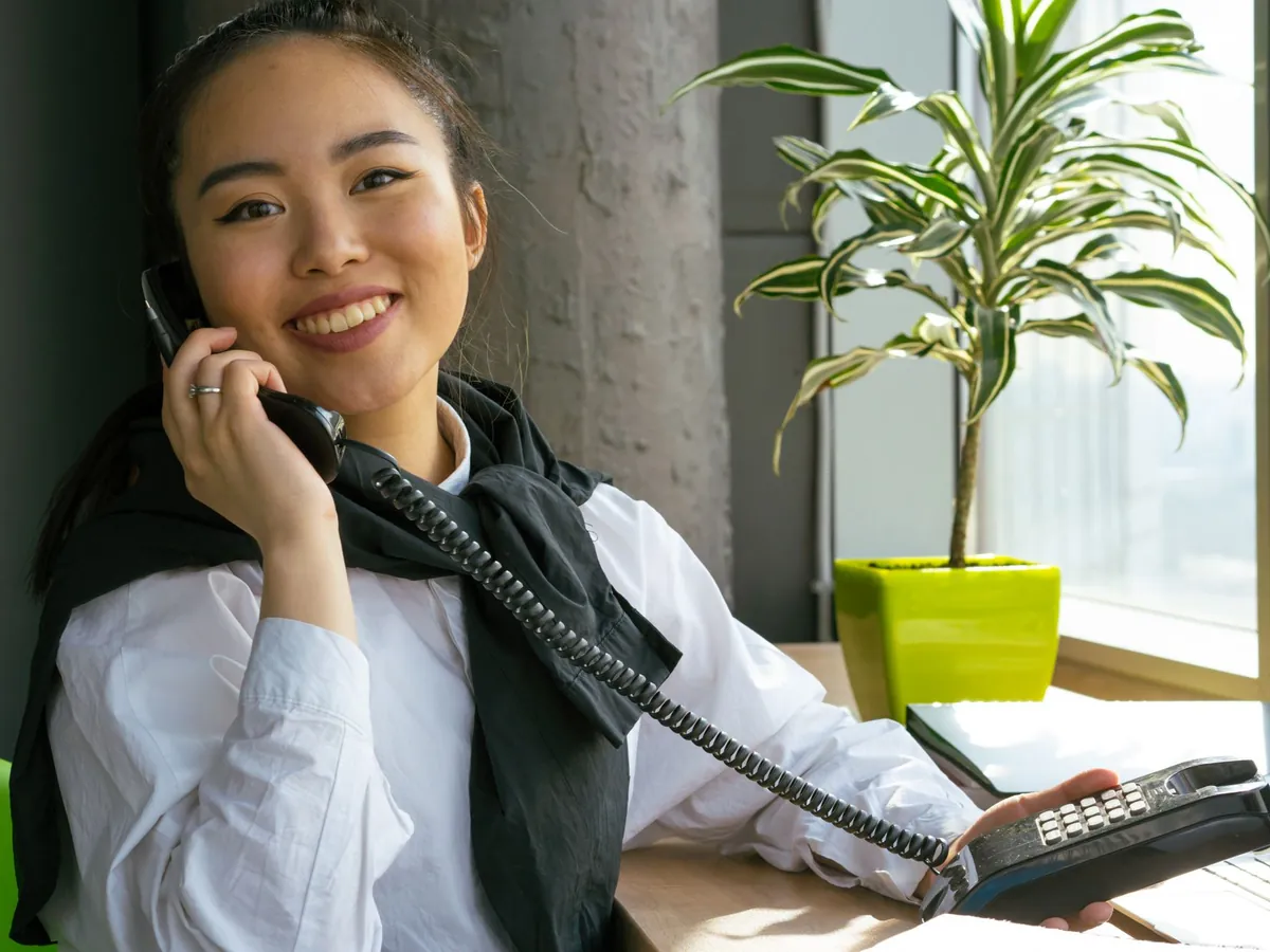 Smiling woman taking a call on a desk phone in a bright office