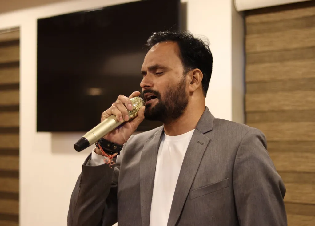 Bearded man in a gray blazer singing low notes into a handheld microphone
